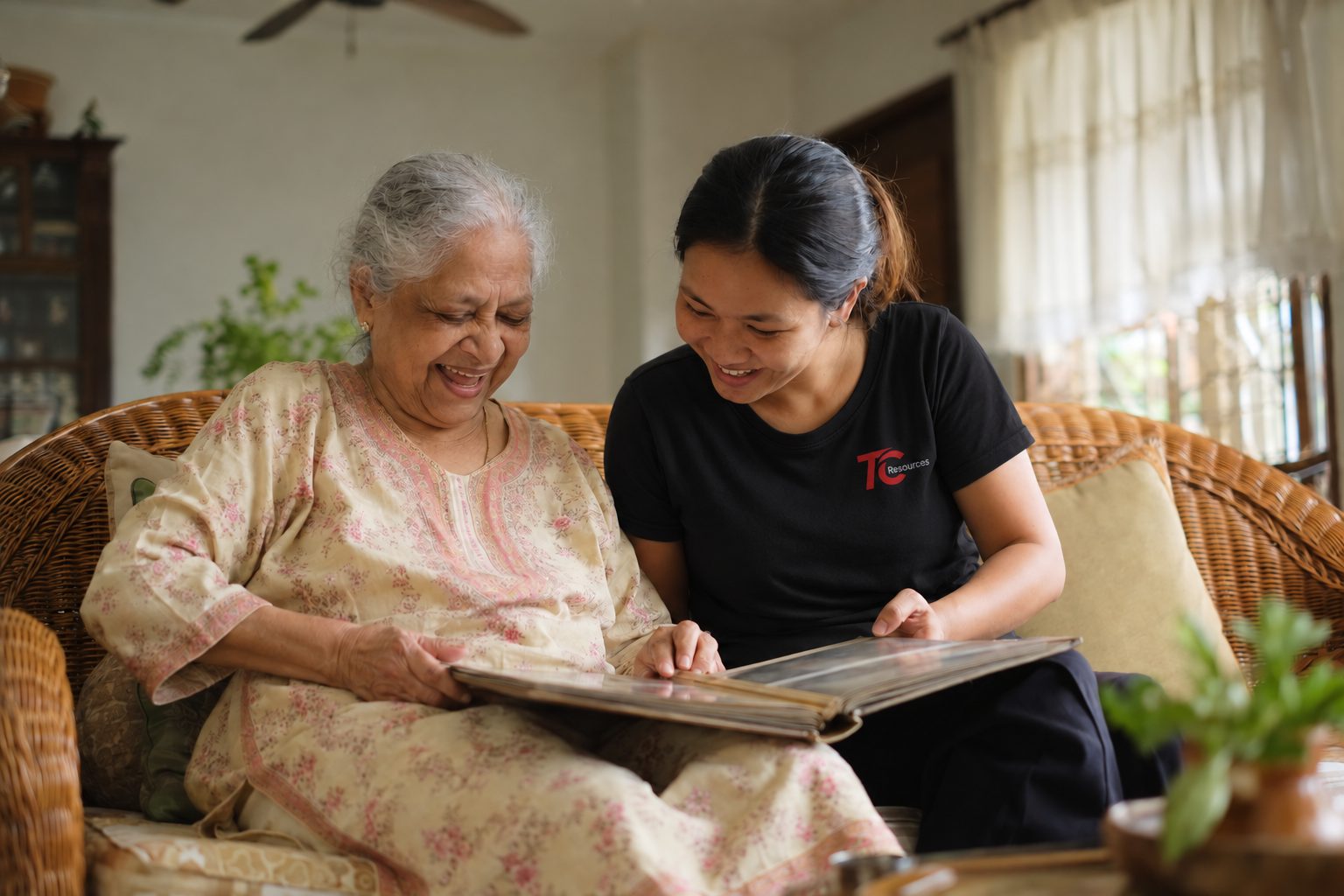 An elderly woman and her helper laughing over a photo album together