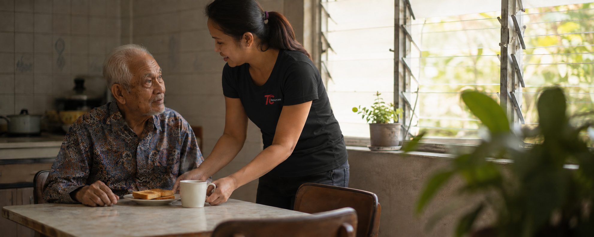A helper serving toast and a hot drink to an elderly man at his kitchen table