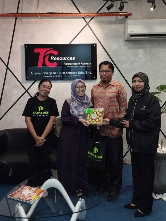 A husband and wife at the TC Resources office with two consultants, standing beneath the agency licence board
